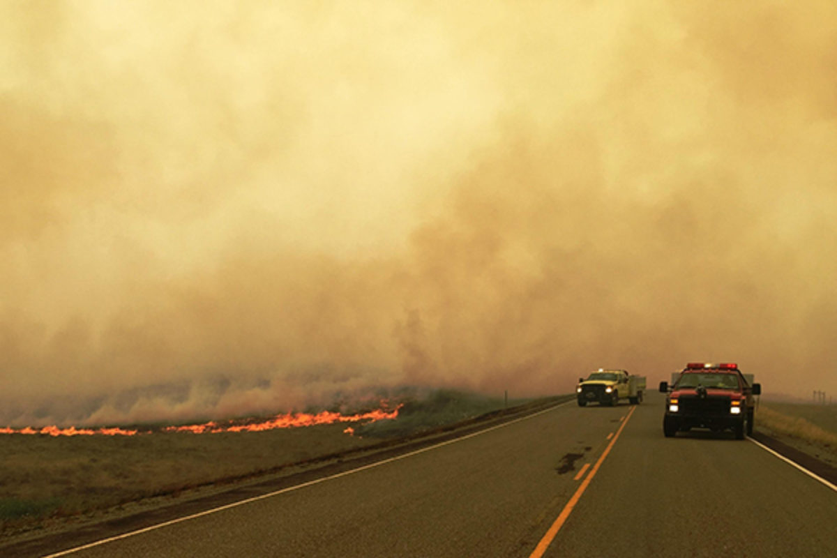 Prairie fire next to road with firetrucks