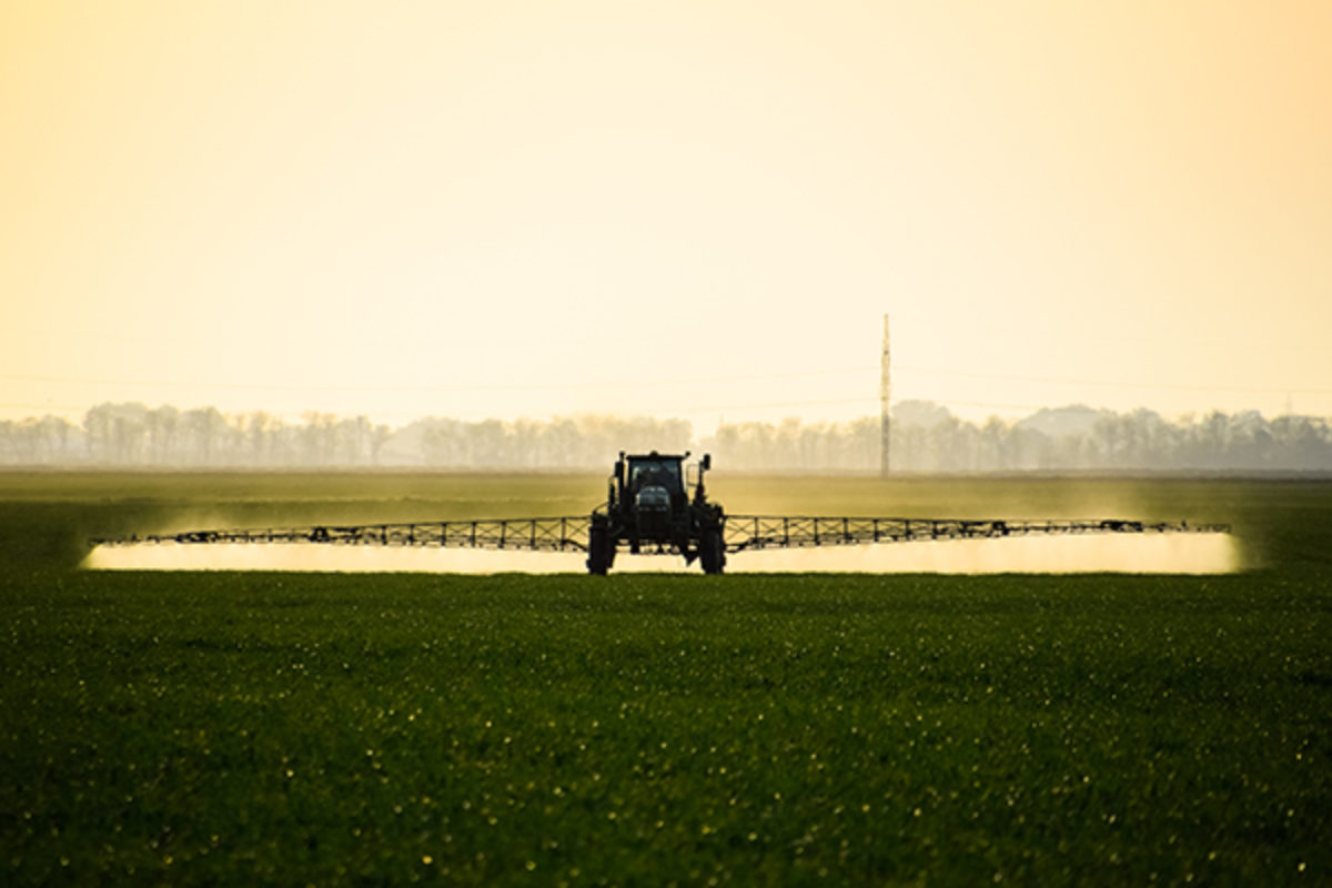 Agricultural equipment spraying field at sunset